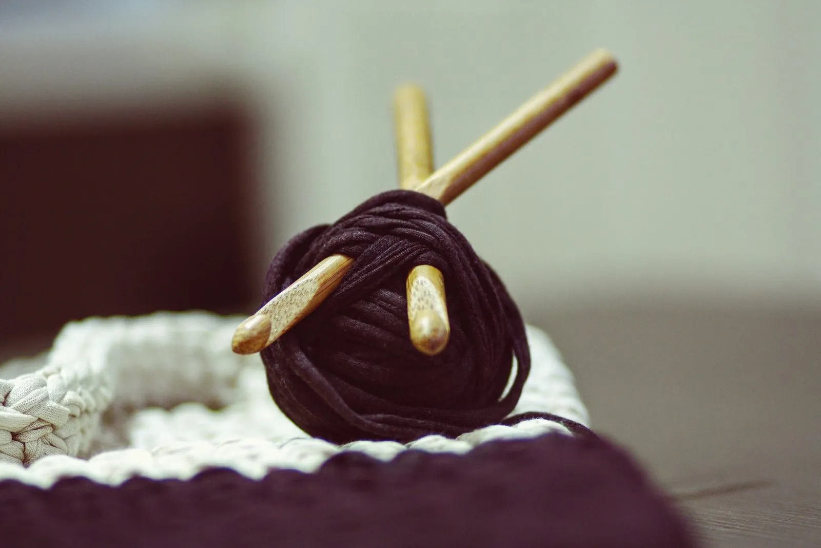 A dark ball of yarn with wooden needles, resting on a knitted white basket